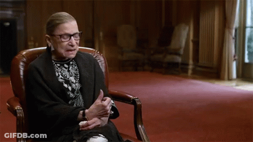 A Woman Sitting In A Chair With Her Hands Folded GIF