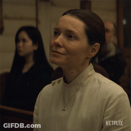 A Woman Sitting In A Church With Netflix Written On Her Sleeve GIF