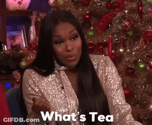 A Woman Sitting In Front Of A Christmas Tree With The Words What 'S Tea Written On Her Face GIF