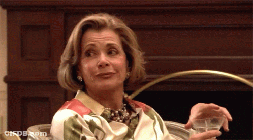 A Woman Sitting In Front Of A Fireplace Holding A Glass Of Water GIF