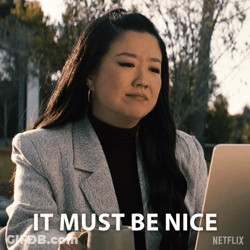 A Woman Sitting In Front Of A Laptop With The Words " It Must Be Nice " On The Bottom Right GIF
