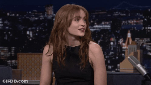 A Woman Sitting In Front Of A Microphone With A City In The Background GIF