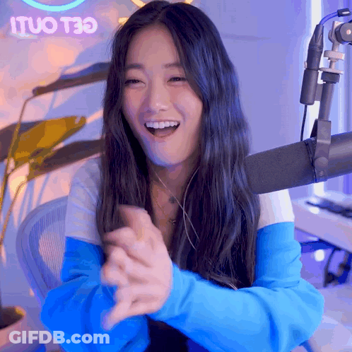 A Woman Sitting In Front Of A Microphone With A Neon Sign That Says Ituo T30 In The Background GIF