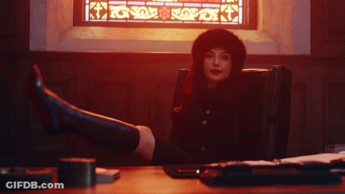 A Woman Sitting In Front Of A Stained Glass Window With Her Feet Up GIF