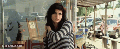 A Woman Sitting In Front Of A Store That Has A Sign That Says Sale On It GIF