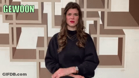 A Woman Sitting In Front Of A Wall That Says Gewoon On It GIF