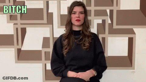 A Woman Sitting In Front Of A Wall With The Word Bitch Written On It GIF