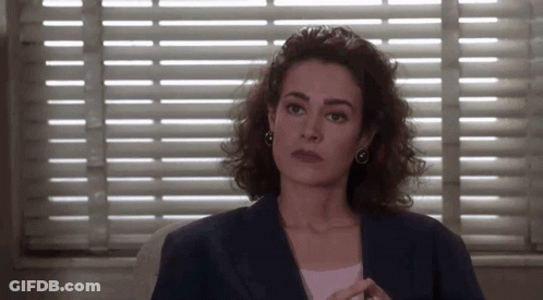 A Woman Sitting In Front Of A Window With Blinds On It . GIF