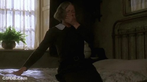 A Woman Sitting On A Bed Covering Her Mouth With Her Hands GIF
