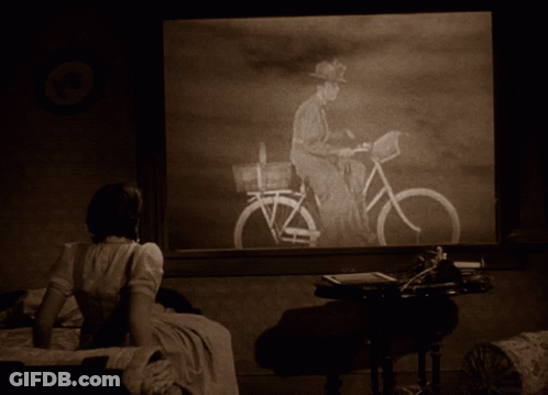 A Woman Sitting On A Bed Looking At A Picture Of A Man On A Bike GIF