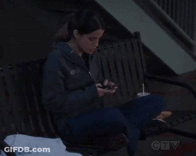 A Woman Sitting On A Bench Looking At Her Phone GIF