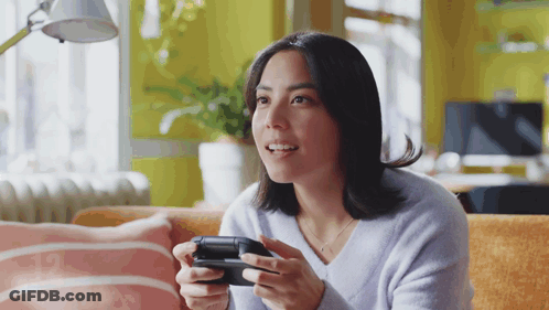 A Woman Sitting On A Couch Holding A Video Game Controller GIF