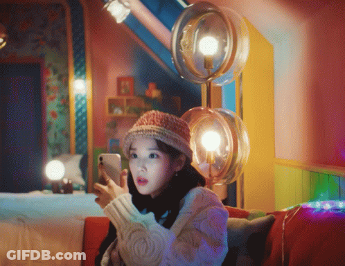 A Woman Sitting On A Couch Looking At A Cell Phone GIF