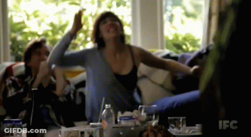 A Woman Sitting On A Couch With Her Arms Outstretched In Front Of A Ifc Sign GIF
