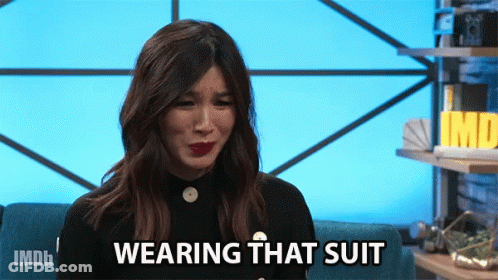 A Woman Sitting On A Couch With The Words " Wearing That Suit " On Her Face GIF