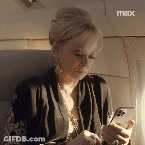 A Woman Sitting On An Airplane Looking At Her Phone With The Max Logo In The Corner GIF