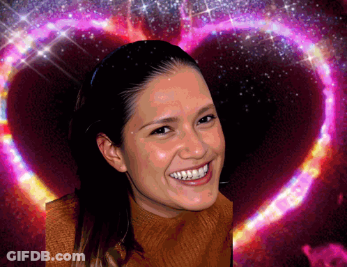 A Woman Smiles In Front Of A Heart Shaped Background GIF