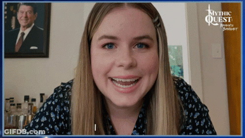 A Woman Smiles In Front Of A Picture Of Ronald Reagan GIF