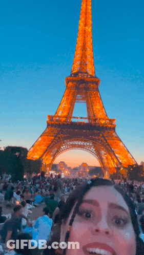 A Woman Smiles In Front Of The Eiffel Tower At Night GIF