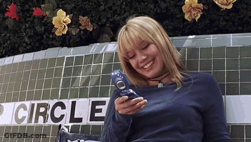 A Woman Smiles While Holding A Cell Phone In Front Of A Sign That Says Circle GIF