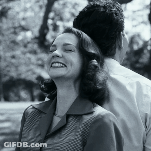 A Woman Smiles With Her Eyes Closed While A Man Holds Her Back GIF