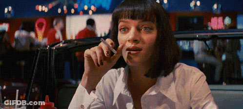 A Woman Smoking A Cigarette In A Diner With A Red Bottle Of Ketchup On The Table GIF