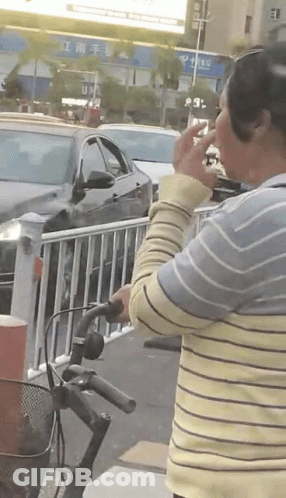 A Woman Smoking A Cigarette While Standing Next To A Bike GIF