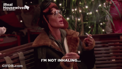 A Woman Smoking A Cigarette With The Words I 'M Not Inhaling Below Her GIF