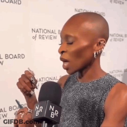 A Woman Speaking Into A Microphone In Front Of A National Board Of Review Wall GIF