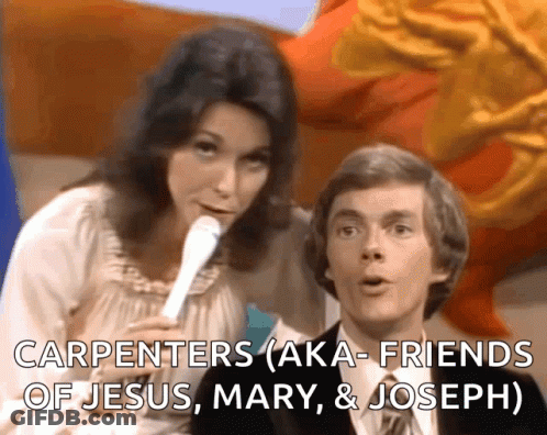 A Woman Speaking Into A Microphone Next To A Man With The Words Carpenters Aka Friends Of Jesus Mary & Joseph GIF