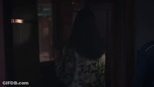 A Woman Standing In A Dark Room Looking Out A Window . GIF