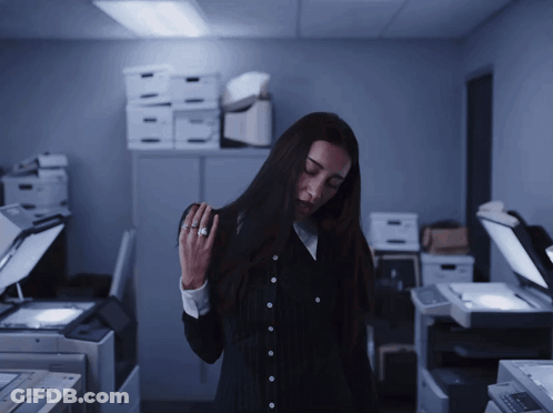 A Woman Standing In A Dark Room With Boxes On The Shelf Behind Her GIF