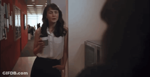 A Woman Standing In A Hallway Holding A Coffee Cup GIF