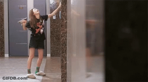 A Woman Standing In A Hallway With A Door That Says Hh GIF