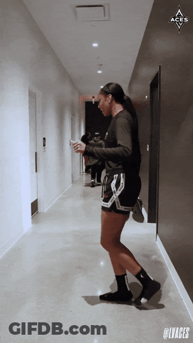 A Woman Standing In A Hallway With The Aces Logo Above Her GIF