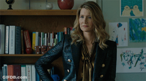 A Woman Standing In Front Of A Bookshelf With A Book Titled Office Minis GIF