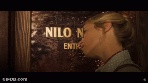A Woman Standing In Front Of A Door That Says Nilo GIF
