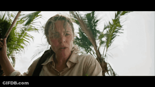A Woman Standing In Front Of A Palm Tree Holding A Stick GIF