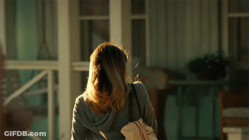 A Woman Standing In Front Of A Porch Holding A Bag GIF