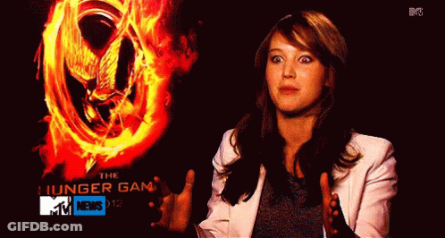 A Woman Standing In Front Of A Poster For The Hunger Games GIF