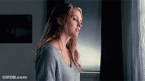 A Woman Standing In Front Of A Window Looking Out GIF