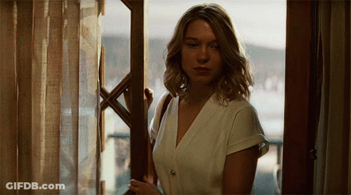 A Woman Standing In Front Of A Window Looking Out GIF