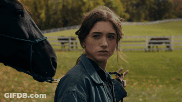 A Woman Standing Next To A Black Horse Looking At The Camera GIF