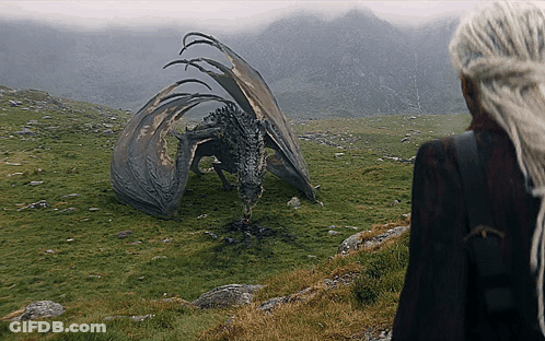 A Woman Standing Next To A Dragon In A Field With Mountains In The Background GIF