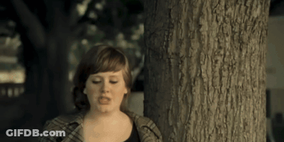 A Woman Standing Next To A Tree With A Serious Look On Her Face GIF