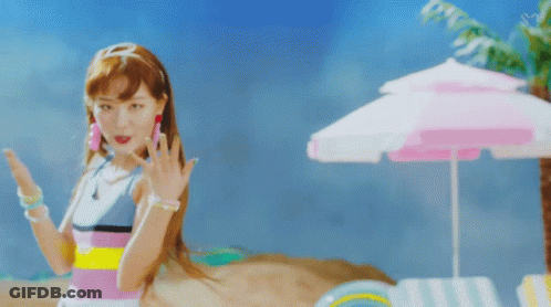 A Woman Standing On A Beach With A Pink Umbrella In The Background GIF