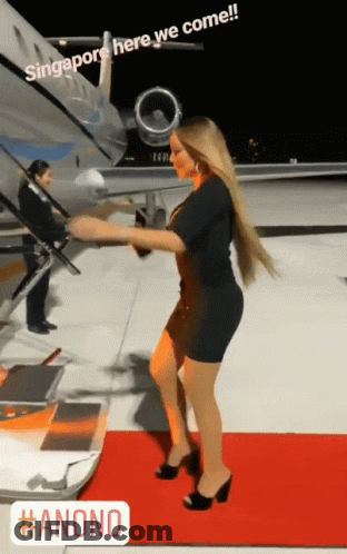 A Woman Standing On A Red Carpet In Front Of An Airplane With Singapore Here We Come Written On It GIF