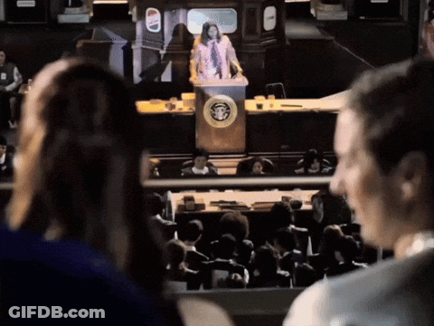 A Woman Stands At A Podium In Front Of A Crowd With A United States Of America Logo GIF