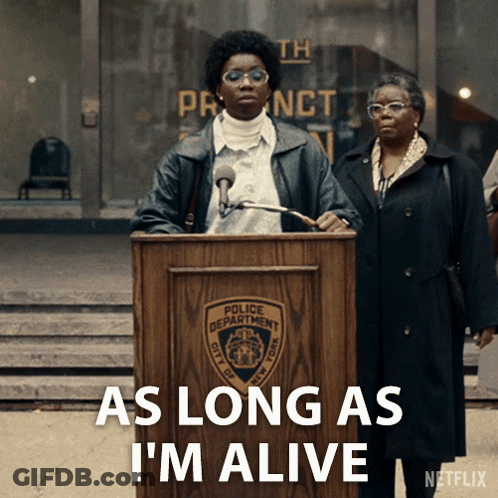 A Woman Stands At A Podium With The Words " As Long As I 'M Alive " Below Her GIF