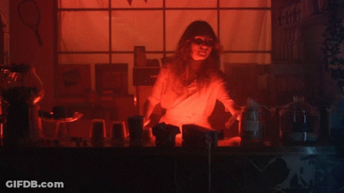 A Woman Stands Behind A Counter In A Dark Room With Purple Lights GIF